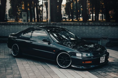 Mașină sport neagră, model clasic, parcat pe trotuar în parc, ideal pentru pasionații de mașini de p.