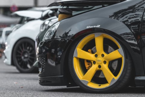 Mașină sport cu jantă galbenă și disc de frână, parcată pe stradă, în fața altor mașini.