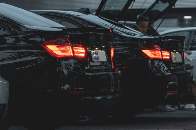 Mașini sport negre în parcare, cu faruri aprinse, într-un mediu urban modern.