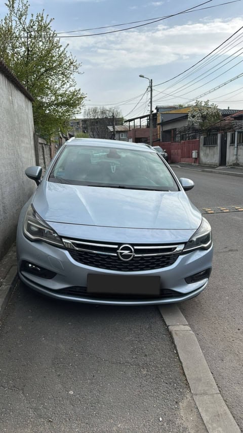Mașină Opel Astra, model modern, în culoare gri, parcat pe stradă urbană, în zona rezidențial.