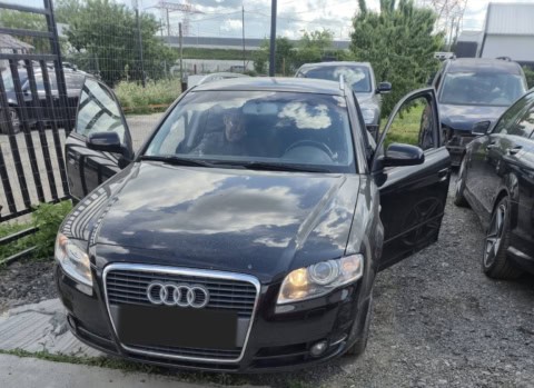 Mașină Audi neagră, parcată în exterior, cu ușa din față deschisă, în zona de depozitare a.