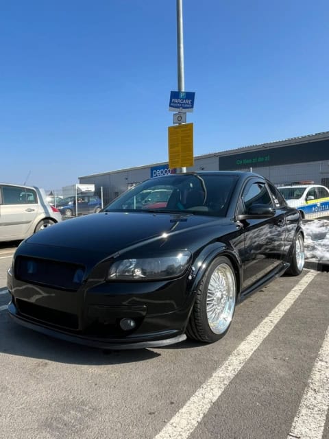 Mașină sport neagră, parcată în parcarea supermarketului, cu roți din aliaj și aspect elegant, în zo.
